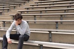 Teenager sitting alone on bleachers, appearing contemplative or distressed, symbolizing the struggle with addiction.